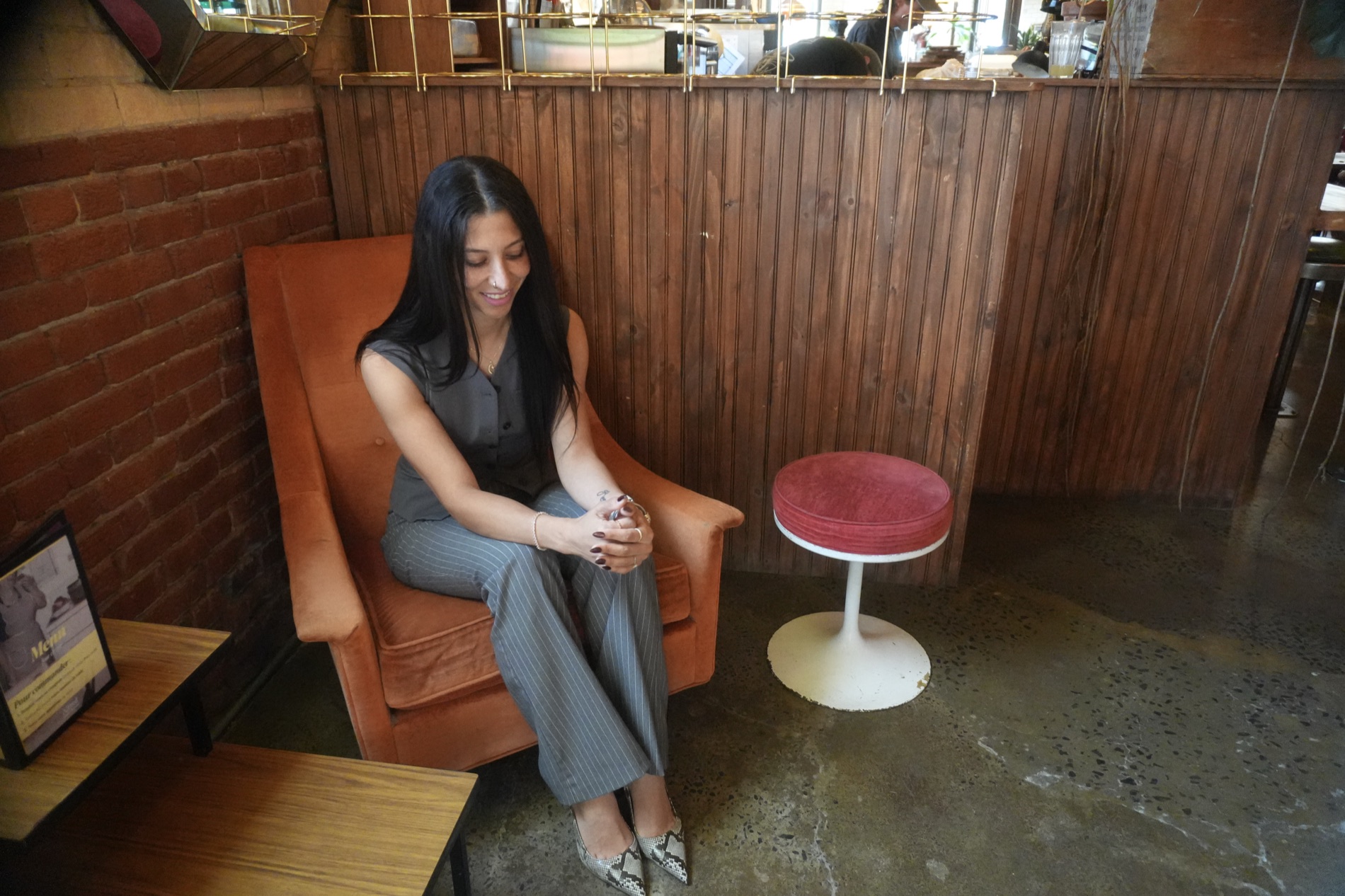 Meryem sitting in an orange velvet armchair, looking down, hands clasped